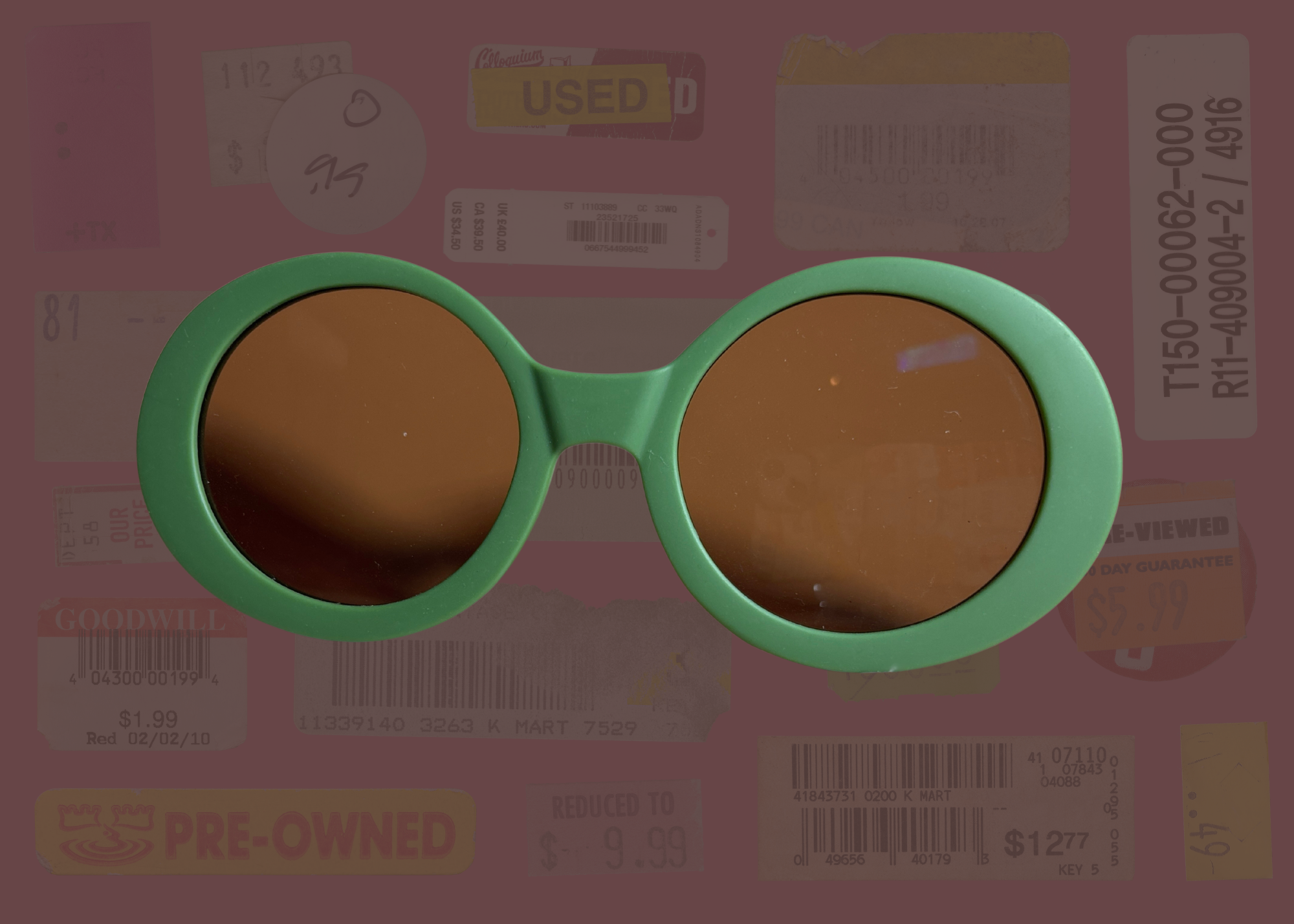 Round green-framed sunglasses with brown lenses on a background of used clothing labels.
